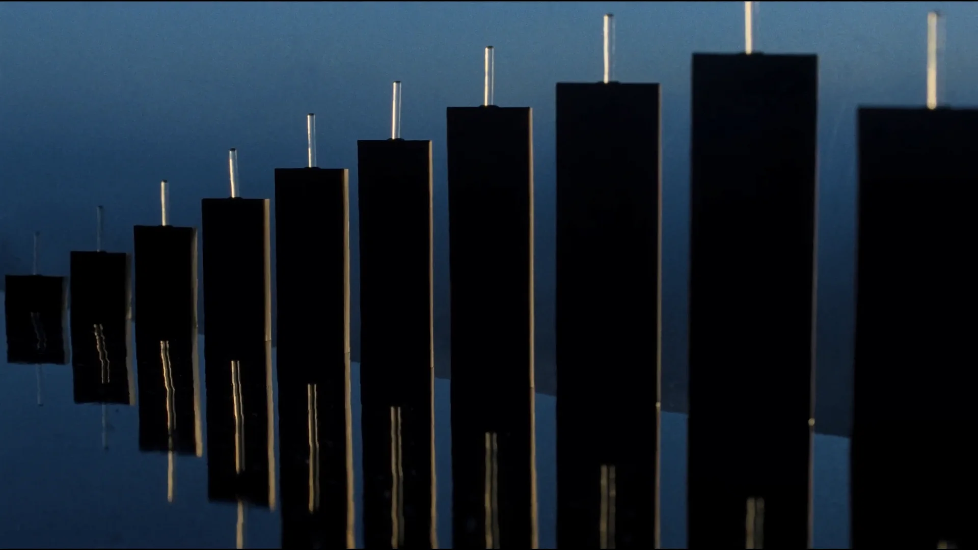 Obsidian candlestick sculptures rising from still black water at first light, edged in gold.
